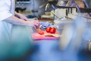 Préparation culinaire dans une cuisine professionnelle avec un chef tranchant une tomate, illustrant la gestion des déchets alimentaires à la source, solution IDS Environnement.