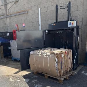 Balle de carton dense et cerclée produite par le Clean Kompact 151 sur palette, devant la presse à balles ouverte, chez Mr.Bricolage Craponne.